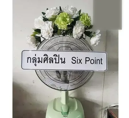 พวงหรีดพัดลมพร้อมป้ายชื่อกลุ่มผู้ส่งและดอกไม้ประดับด้านบน สำหรับงานบำเพ็ญกุศลศพพระ